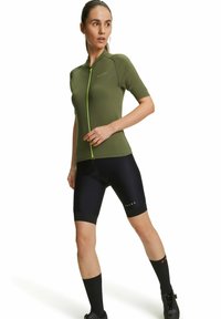 Maglia da ciclismo verde a maniche corte con una zip frontale e dettagli in verde neon a contrasto, abbinata a pantaloni corti da ciclismo neri e calze.