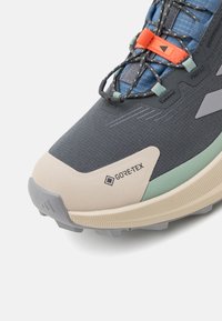 Buty do wędrówek GORE-TEX w czarno-szarym kolorze z jasnoszarym wierzchem, zielonymi akcentami, teksturowaną powierzchnią oraz trwałą gumową podeszwą z wyraźnymi bieżnikami.