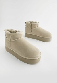 Bottines beige avec une finition en daim lisse, doublure en polaire douce et semelle plateforme. Comprend une fermeture éclair sur le côté pour un enfilage facile.