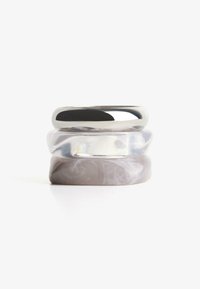 Három gyűrűből álló halom: egy ezüstszínű fémgyűrű, egy áttetsző, tiszta gyűrű, és egy márványozott szürke gyűrű világos forgókkal és sima felülettel.