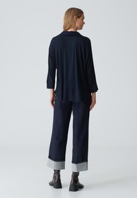 Maglietta a maniche lunghe blu navy con colletto, abbinata a pantaloni in denim scuri con orlo risvoltato e accenti grigi, indossata con stivali alla caviglia.