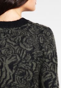 Dzianinowy sweter w ciemnozielonym i czarnym kolorze z teksturowanym wzorem róży. Posiada okrągły dekolt i miękki, puszysty materiał.