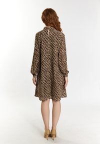Robe brune avec un motif texturé de boucles couleur crème, dotée de manches longues, d'un col haut et d'un détail en forme de trou de serrure au dos.