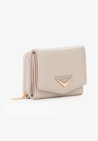 Portafoglio in pelle beige compatto con cerniera dorata e targhetta metallica triangolare sul risvolto anteriore, esposto su sfondo bianco.