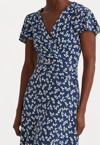 Blommig omlotklänning i marinblått, med korta volangärmar och midja med resår. Tyget har vita blommönster över hela.