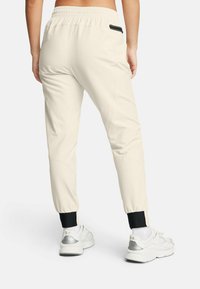 Cream-colored joggers with an elastic waistband and black cuffs. Features a subtle sheen and a zipper pocket on the back.