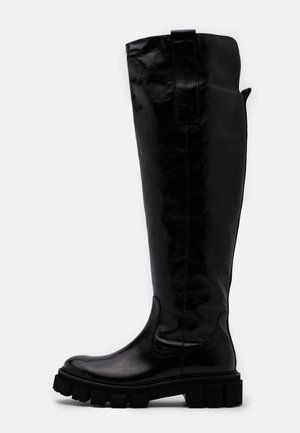 Bottes noires hautes en cuir brillant, avec une finition texturée, des semelles en caoutchouc noir épaisses et une languette en haut.