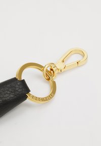 Schwarzes Lederarmband mit einer goldfarbenen Metallverschluss. Der Verschluss verfügt über einen runden Ring, der mit "Coccinelle" graviert ist. Glatte Texturdetails sind sichtbar.