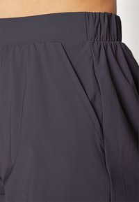 Dark gray, lightweight fabric pant featuring an elastic waistband, tapered design, and slanted side pockets with subtle stitching details.