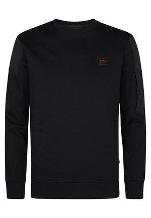 Sudadera negra hecha de tela texturizada, con cuello redondo, puños acanalados y un parche con el logo en el pecho. Bolsillo lateral con detalle de cremallera.