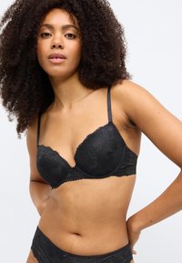 Čierna čipkovaná podprsenka s tvarovanými košíčkami, nastaviteľnými ramienkami, kvetinovými vzormi a vlnitými okrajmi, doplnená o zodpovedajúce čipkované nohavičky.