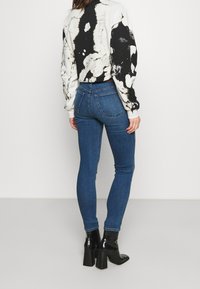 Tunna blå denimjeans med midjehöjd, med en klassisk femfickdesign och subtila slitningar. Matchas med en svartvit mönstrad topp.