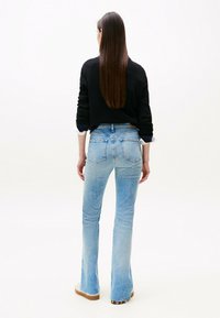 Jeans a zampa d'elefante di colore blu chiaro con un lavaggio sbiadito, tasche posteriori dettagliate, orlo sfilacciato, abbinati a un maglione nero corto con polsini bianchi.