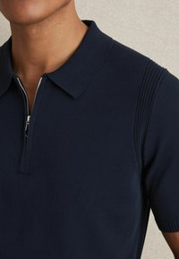 Námořnická polo košile s límcem na zip, žebrovanými rukávy a texturovanými bočními panely. Vyrobena z hladkého materiálu.