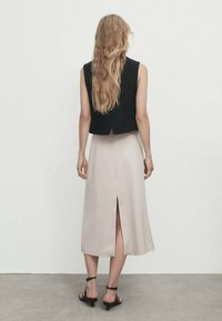 Black cropped sleeveless top and light beige satin midi skirt with a rear slit, worn with black strappy sandals, viewed from behind.