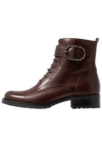 Bottine en cuir marron avec bout arrondi, design à lacets latéraux, sangle décorative avec boucle métallique et semelle noire texturée.