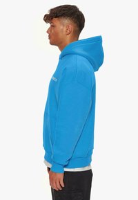 Blaues Kapuzensweatshirt mit Kängurutasche und gerippten Bündchen. Verfügt über ein einfaches Logo auf der Vorderseite und einen weichen, strukturierten Stoff.