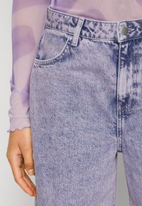 Violetti tye-dye farkut, joissa on korkea vyötärö, viisi taskua ja hieman haalistunut pinta, varustettuna metallinappisulkimella.