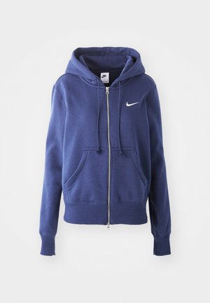 Marine blå hettegenser med glidelås laget av mykt stoff, med en frontlomme, ribbestrikkede mansjetter og en hvit Nike-logo på brystet.