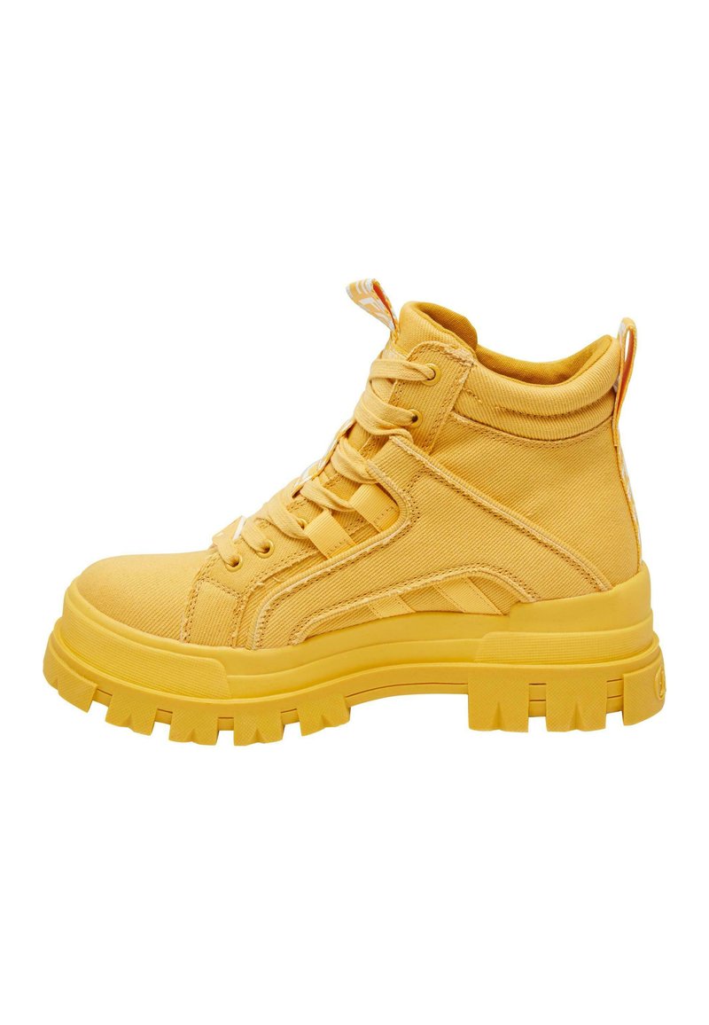 Zapatillas amarillas de caña alta, hechas de lona, con una suela gruesa, cordones en la parte frontal y un tirador en la parte trasera. Tela texturizada con rayas.
