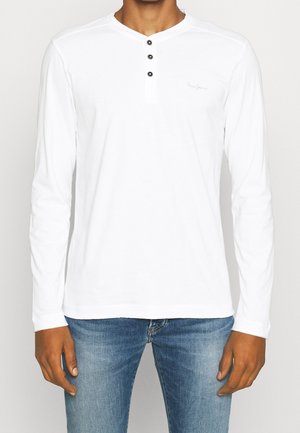 T-shirt blanc à manches longues avec un col henley, trois boutons noirs et un détail de logo subtil sur la poitrine. Fabriqué en tissu doux.