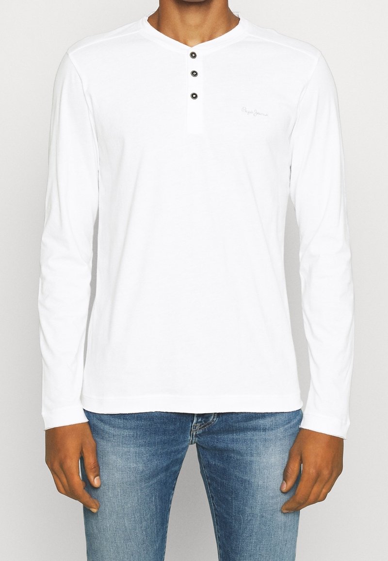 Biała bluza z długim rękawem z dekoltem henley, z trzema czarnymi guzikami i subtelnym detalem logo na piersi. Wykonana z miękkiego materiału.