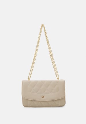 Beige gewatteerde handtas met flap en klein gouden embleem, met een lange gouden kettingriem voor schouder- of crossbody-dracht.