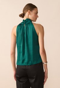 Satin halter topp i dyp smaragdgrønn med en samlet halslinje og nøkkelhullsdetalj bak. Glatt tekstur og tettsittende silhuett.