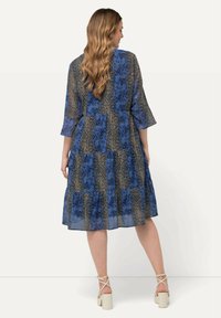 Sininen, kukkakuosisella mekolla on kerroksellinen muotoilu, kolmannes hihan pituus ja vartalonmyötäinen siluetti. Valmistettu kevyestä, läpinäkyvästä kankaasta.