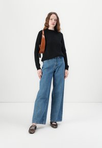 Svart tröja, ljusblå vida jeans, brun lädercrossbody-väska med ett texturerat mönster och svarta skor med leopardmönster.