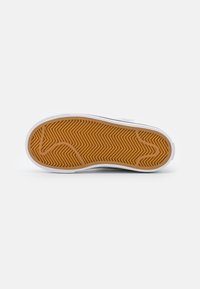 Sole of a sneaker featuring a gum rubber outsole with a zigzag pattern and a white midsole. Smooth texture and rounded shape.