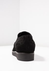 Scarpa in suede nero con perforazioni decorative e punta tonda. Presenta un tacco in gomma nera bassa e un colletto aderente. Design semplice, texture liscia.