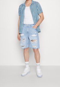 Lyhythihainen sinivalkoinen ruudullinen paita valkoisen topin päällä, yhdistettynä vaaleansinisiin kulutettuihin farkkushortseihin ja valkoisiin tennareihin.