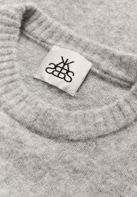 Lysegrå strikket sweater med ribbet krave og hvidt stofplejeetiket syet ind i halsudskæringen.