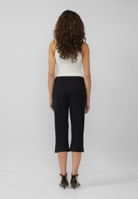 Zwarte cropped broek met een getailleerde pasvorm, voorzien van een soepele textuur en discreet achterzakken, gecombineerd met zwarte höghe hielen.