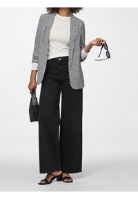 Blazer de pata de gallo en blanco y negro sobre una blusa blanca, combinado con pantalones negros de pierna ancha y sandalias de tacón bloque negro, sosteniendo unas gafas de sol y un bolso.