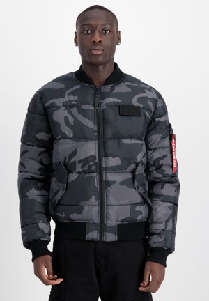 Veste bombardier matelassée en camouflage noir et gris, avec une fermeture éclair devant, des poignets côtelés et un patch logo sur la poitrine.