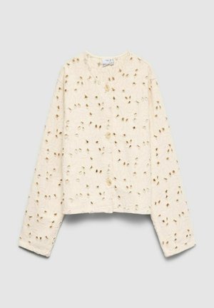 Blouse crème à manches longues boutonnée avec broderie florale ajourée et col rond sur fond uni clair.