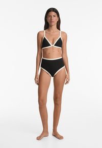 Fekete bikini szett, amelynek háromszög alakú melltartója van krémszínű kiegészítőkkel és magasan szabott alsórésszel. Simább textúrájú, egyszínű dizájn.