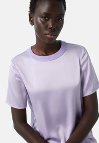 Světle fialová krátká rukávová košile s kulatým výstřihem. Hladká textilie a jednoduchý design, vhodné pro volný čas.