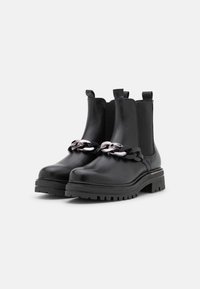 Bottes noires en cuir avec une semelle épaisse, dotées de panneaux latéraux élastiques et d'une chaîne en métal argenté décorative à l'avant.