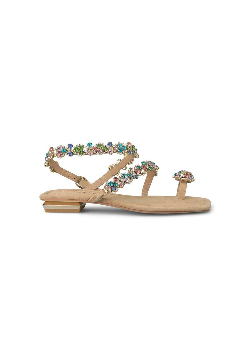 Sandalias planas beige con tiras joyadas que presentan piedras multicolores. El diseño incluye un pequeño lazo para el dedo del pie y un tacón cuadrado con acentos dorados.