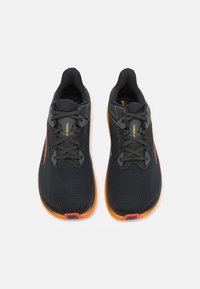 Chaussures de sport noires avec des accents oranges, tige en tissu maillé, semelle rembourrée et lacets plats; présentant des motifs texturés et des détails de marque.