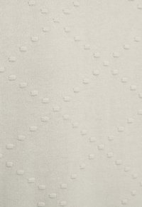 Off-white stickad tyg med ett strukturerat diamantmönster av små upphöjda prickar jämnt fördelade.