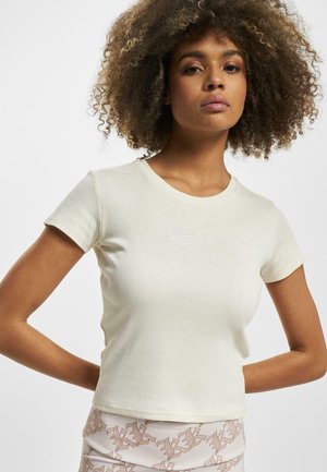 T-shirt côtelé beige clair à manches courtes et col rond. Présente un logo brodé discret sur la poitrine. Texture lisse.