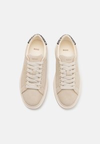 Pair of beige suede sneakers with cream laces, branded "BOSS" on tongue, side, and insole, featuring dark patterned heel accents.