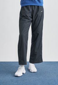 Μαύρο, ελαφρύ παντελόνι φόρμας με φερμουάρ στο πλάι και λογότυπο Nike· συνδυασμένο με λευκά αθλητικά παπούτσια. Ύφασμα με επίπεδη και λεία υφή.