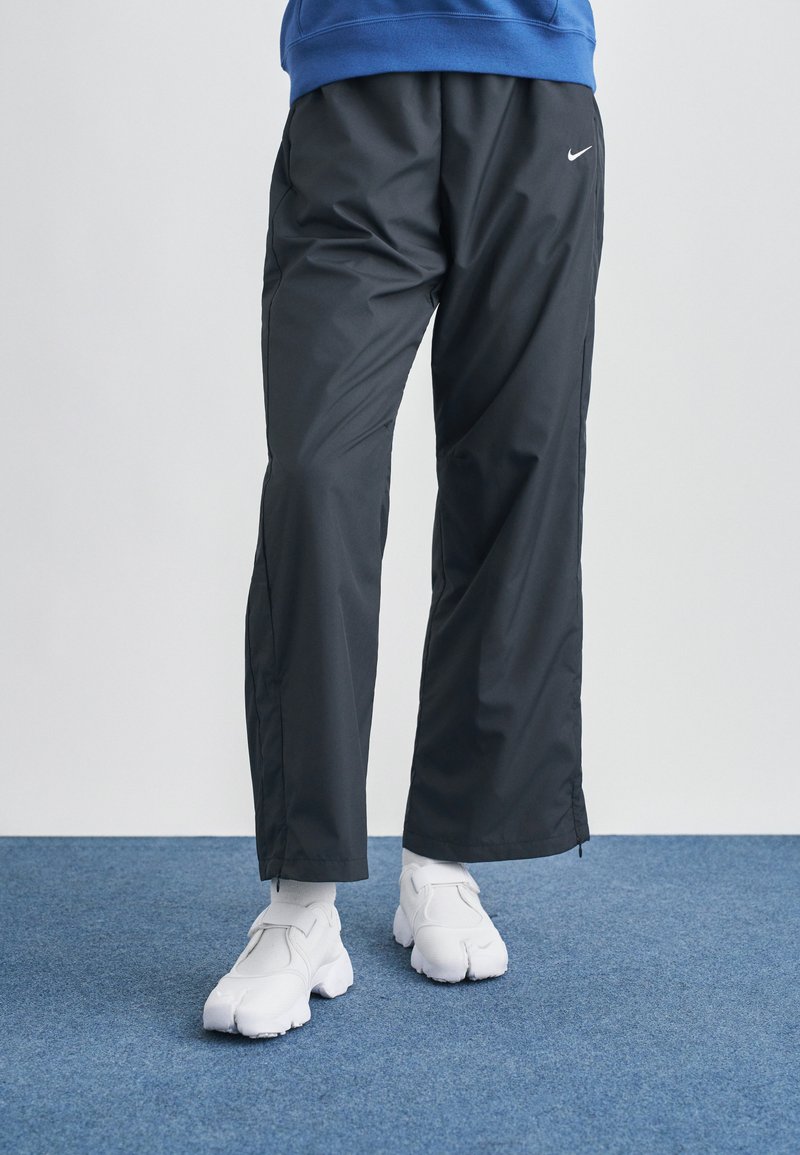 Μαύρο, ελαφρύ παντελόνι φόρμας με φερμουάρ στο πλάι και λογότυπο Nike· συνδυασμένο με λευκά αθλητικά παπούτσια. Ύφασμα με επίπεδη και λεία υφή.