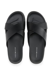 Black sandals with a cross-strap design, made of smooth and textured synthetic materials. Flat sole with subtle branding detail.