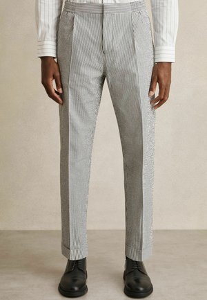 Pantalons rayés en blanc et marine, avec une coupe ajustée, un devant plissé et des ourlets à revers, associés à des chaussures noires à lacets.
